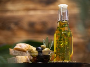 Olives and bottle of olive oil on wooden background, close up